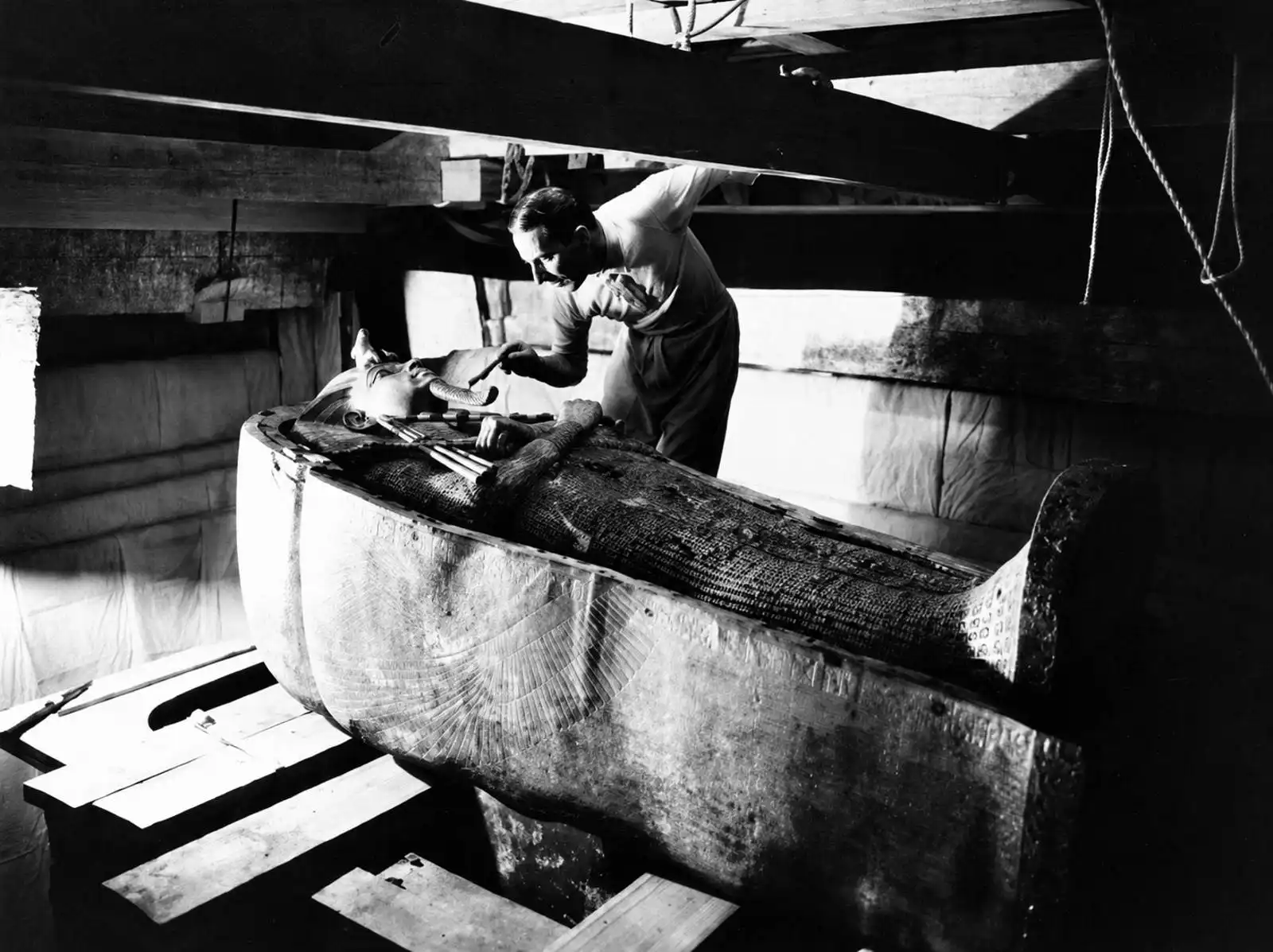 Howard Carter při průzkumu nejvnitřnější zlaté rakve faraona Tutanchamona. Fotografie zachycuje jeden z nejvýznamnějších okamžiků archeologického výzkumu hrobky. Foto: Harry Burton.