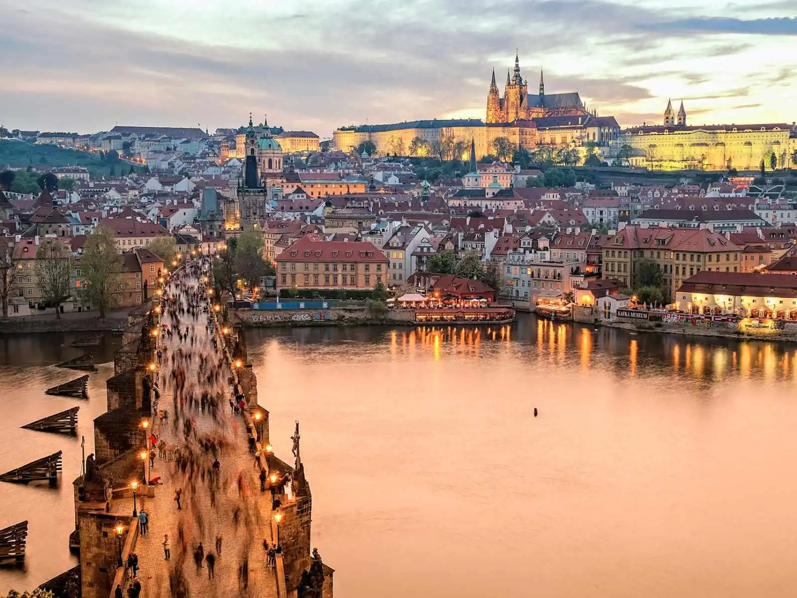 Panoramatický pohled na historickou Prahu s Karlovým mostem, Vltavou a Pražským hradem při západu slunce.